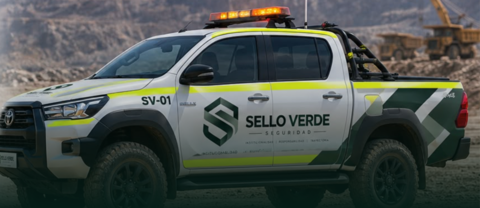 Tres camionetas de escolta Sello Verde blancas con franja verde, balizas encendidas y logo en las puertas, en una faena minera al anochecer
